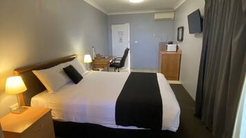 Habitación de hotel con cama, escritorio, silla, televisión y ventana con cortinas.