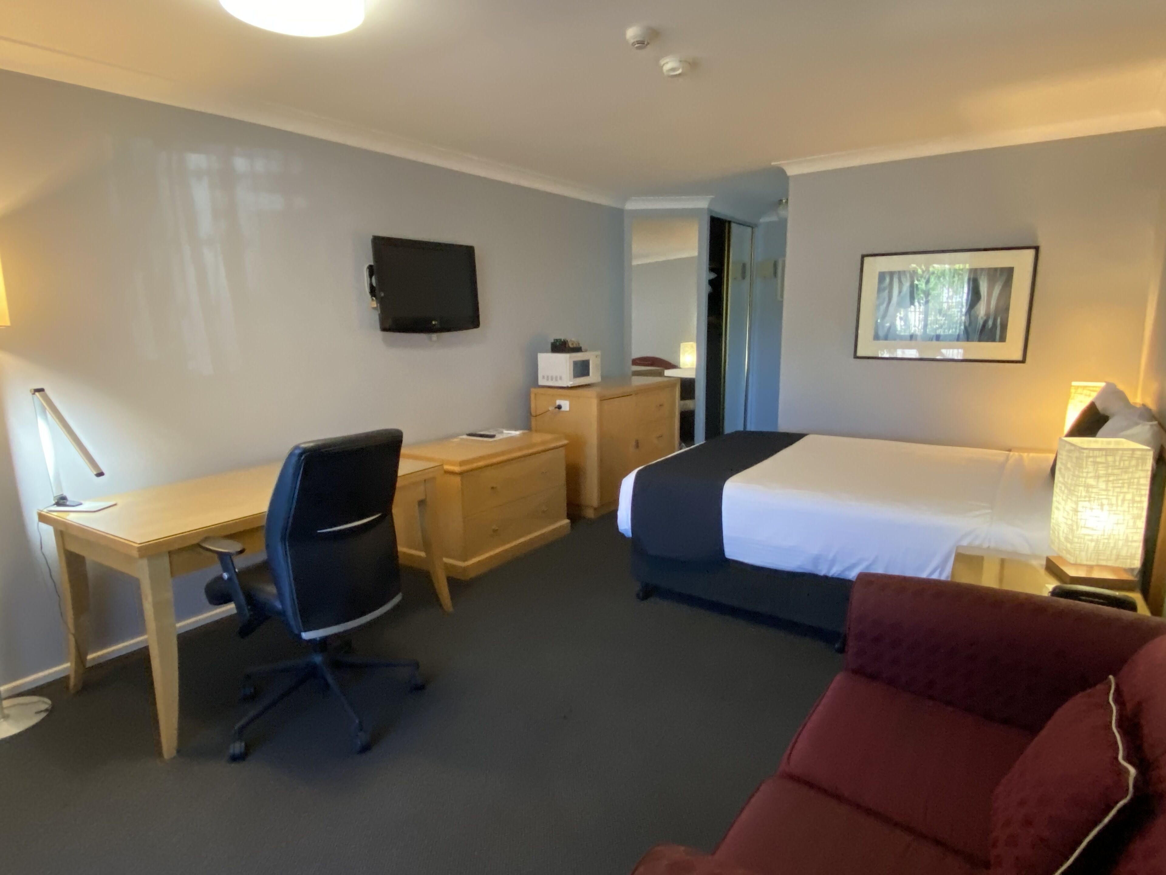 A hotel room with a bed, desk, chair, and a television on the wall.