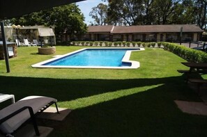 Une piscine entourée d’une pelouse bien entretenue, avec des chaises longues et une table de pique-nique.