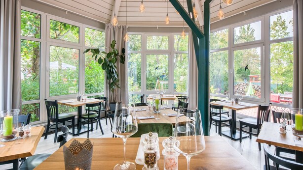 A restaurant with multiple tables and chairs, large windows, and hanging light fixtures.