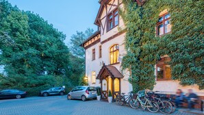 A traditional building with ivy-covered walls, a brick driveway, and bicycles parked outside.