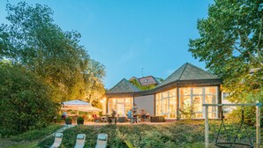 A house with a large glass conservatory, outdoor seating area, and a swing set.