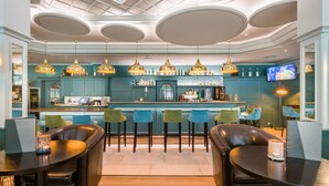 A bar area with teal cabinetry, multiple bar stools, and pendant lighting.