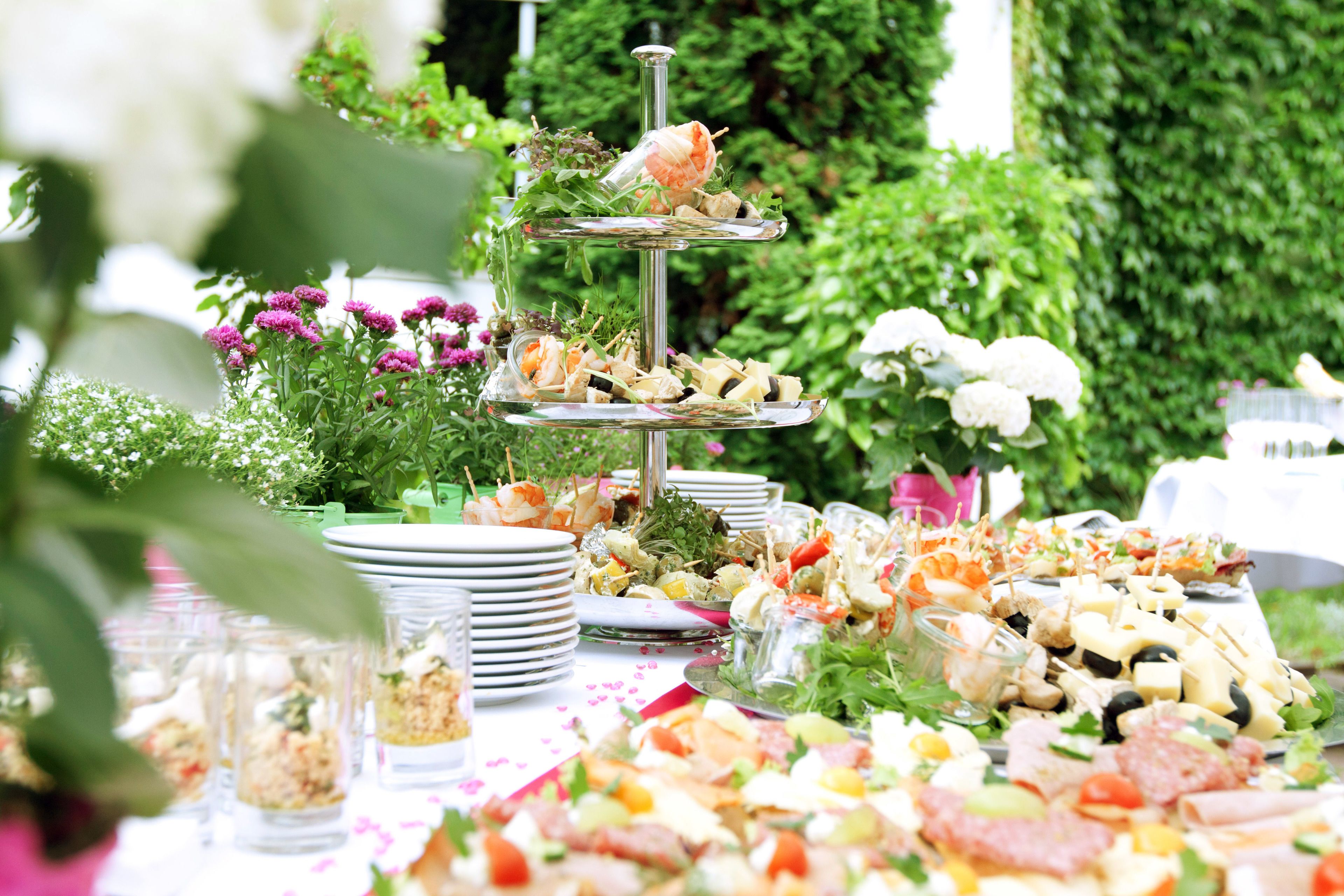 A multi-tiered appetizer stand with various food items and a floral arrangement in the background.