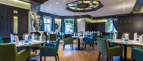 Un restaurant au décor moderne, avec des chaises recouvertes d’un tissu vert, des tables en bois et un plafond décoratif.