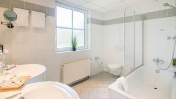 A modern bathroom with a bathtub, a toilet, a sink, and a window.