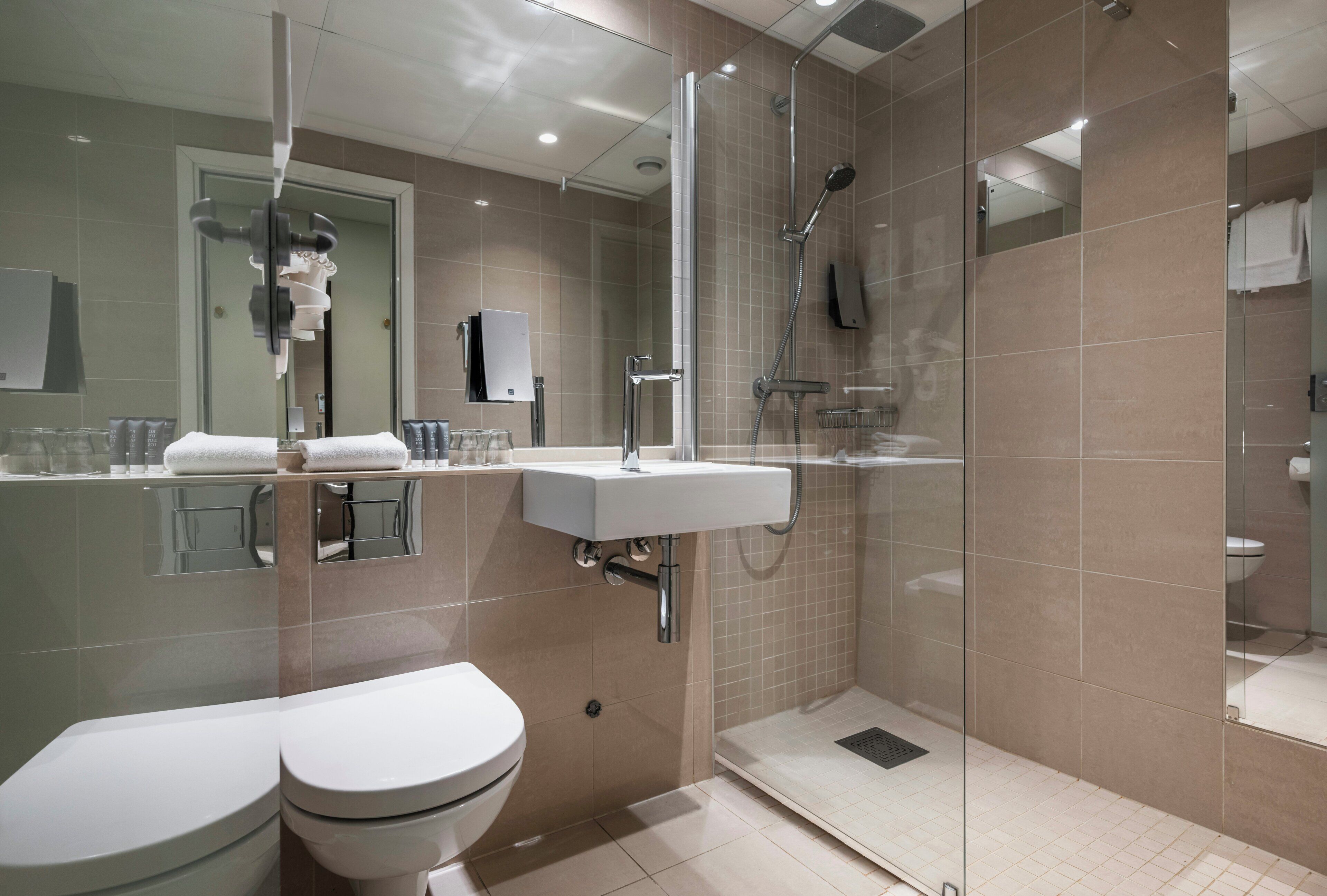 A modern bathroom with a glass-enclosed shower, a white sink, and two toilets.