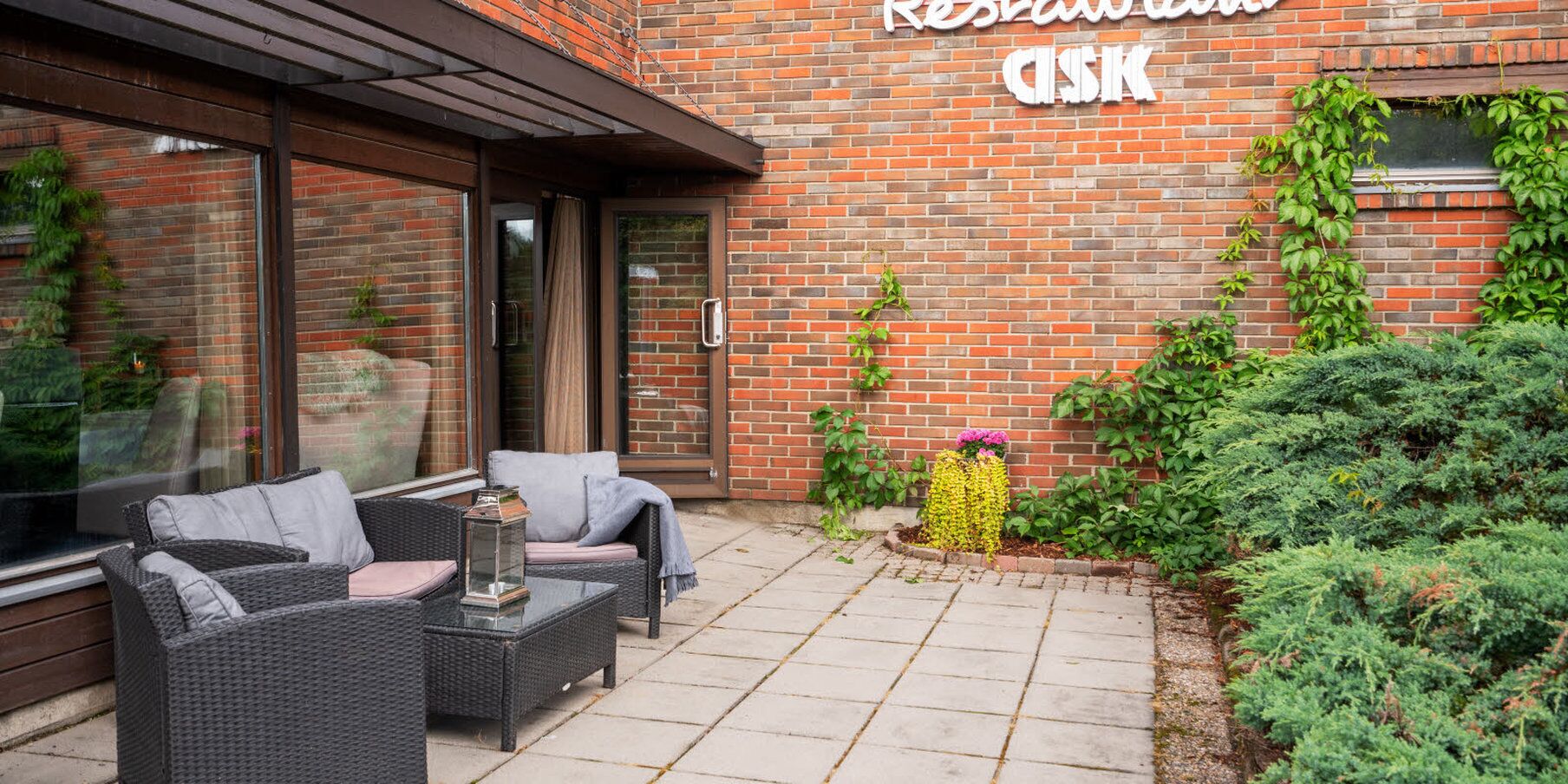 Un espace extérieur aménagé avec des meubles en osier et un mur de briques sur lequel est apposée une enseigne indiquant « Résidence ASK ».