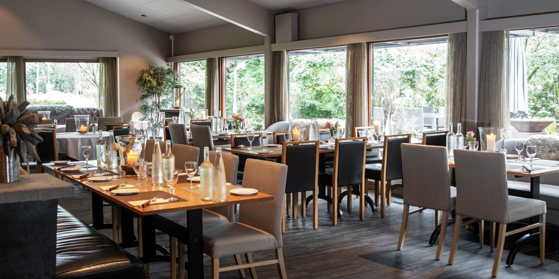 Un restaurante moderno con amplios ventanales, mesas y sillas de madera.