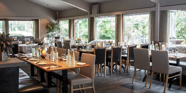 Un restaurante moderno con amplios ventanales, mesas y sillas de madera.