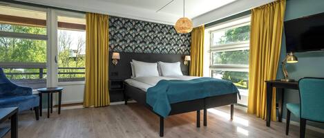 A bedroom with a bed, a desk, a chair, a TV, and large windows with curtains.