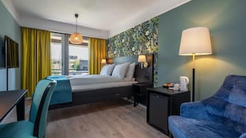 Habitación de hotel con cama, escritorio, silla, lámpara y vistas al exterior.