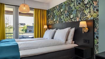 Habitación de hotel con una cama grande, cortinas amarillas, un papel tapiz estampado y vistas al exterior.