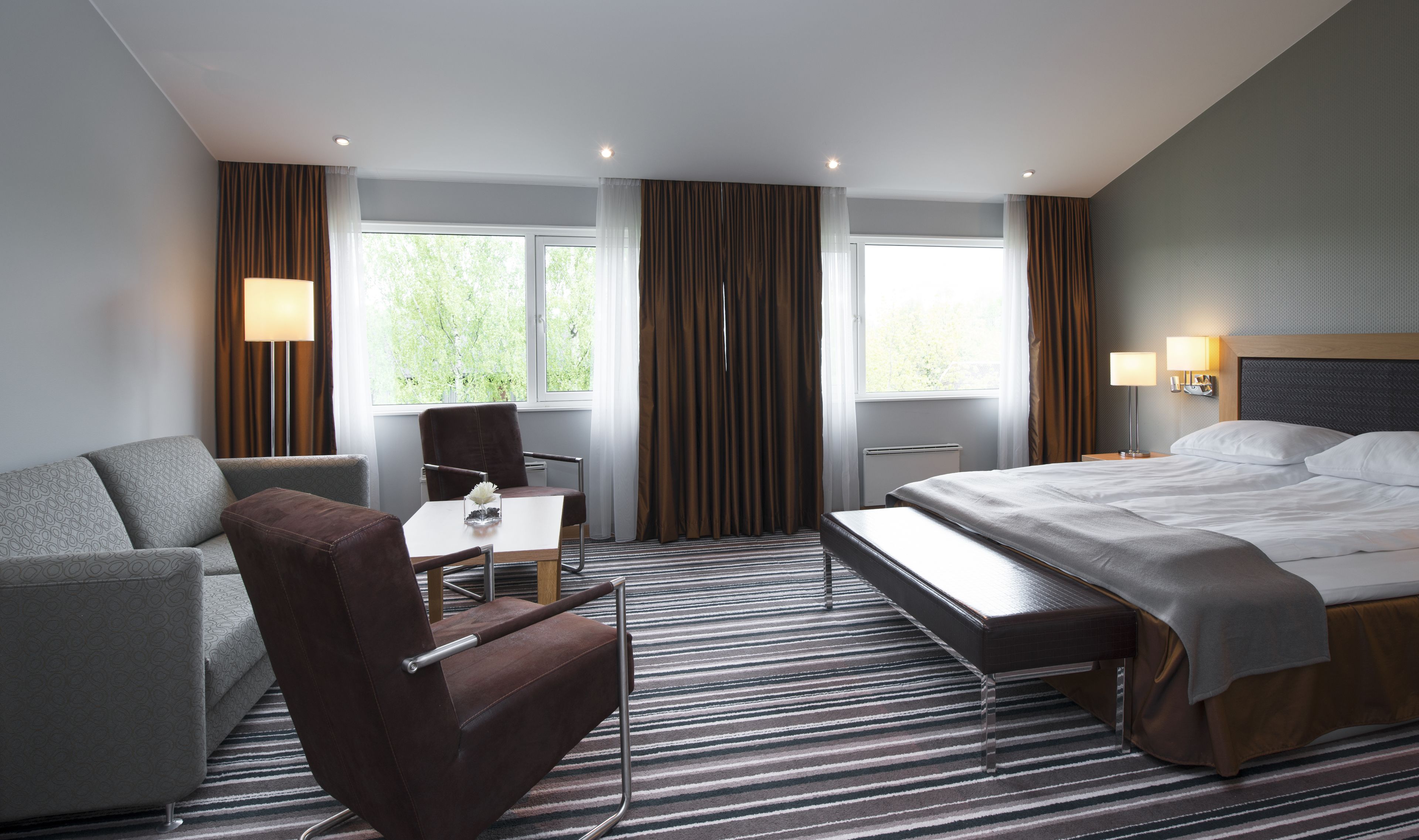 A hotel room with a bed, a sofa, a chair, a table, and a window with curtains.