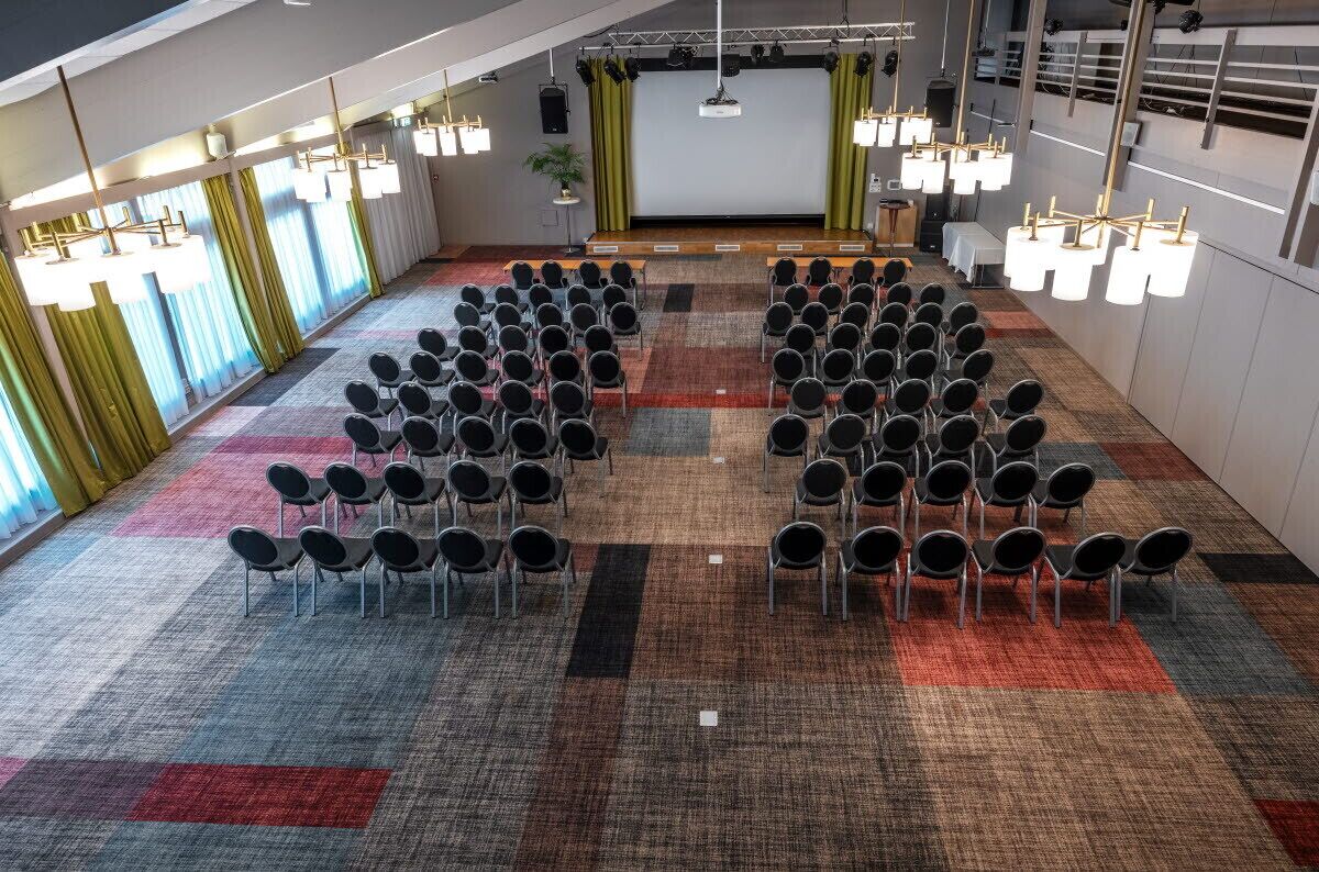 A conference room with rows of chairs, a stage, and a carpeted floor.