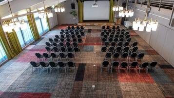 A conference room with rows of chairs, a stage, and a carpeted floor.
