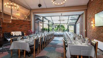 A long dining table set for a meal, with a brick wall and a glass enclosure in the background.