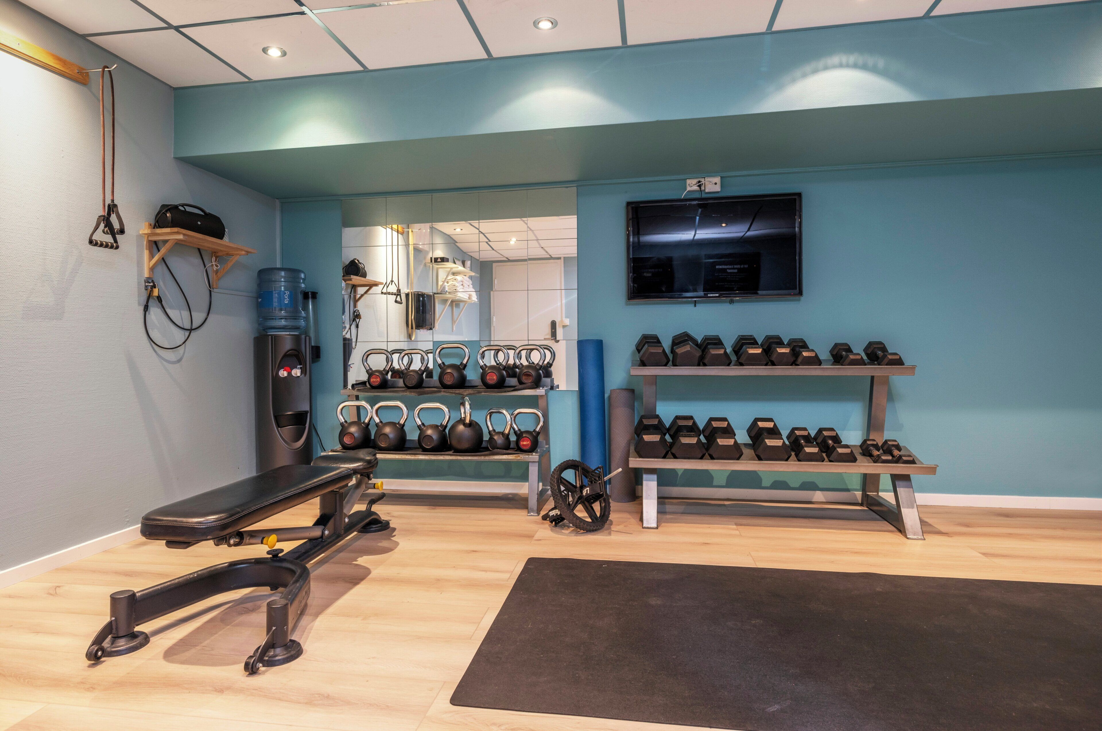 A gym with a bench, kettlebells, dumbbells, and a water dispenser.