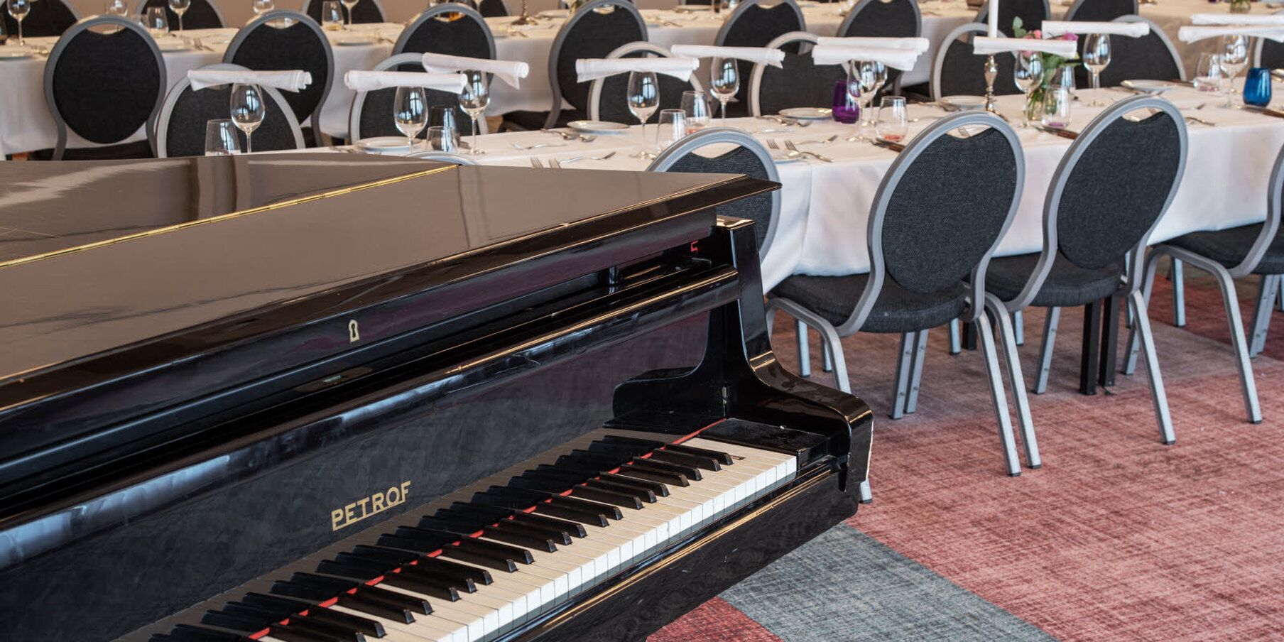 Un piano de cola en un elegante comedor con mesas y sillas redondas.