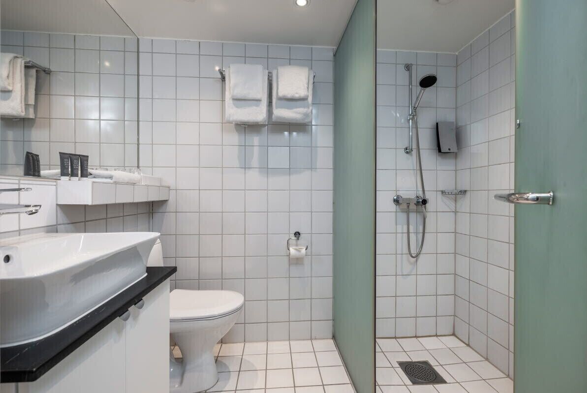 Un baño moderno con inodoro blanco, lavamanos con encimera negra y zona de ducha con puerta de cristal.