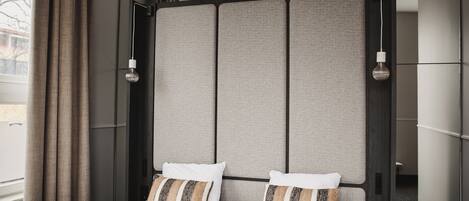 A modern hotel room with a large bed, two pillows, a headboard with a textured panel, and a hanging light fixture.