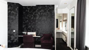 Et moderne hotelværelse med en seng, et skrivebord med stol, et badeværelse der kan ses gennem en åben dør, og et stort spejl.