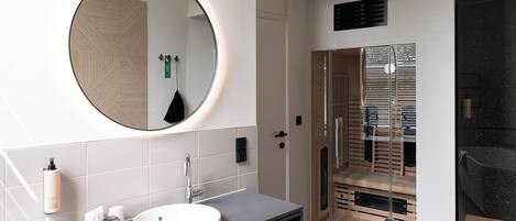 A modern bathroom with a round mirror, a sink, and a shower area.