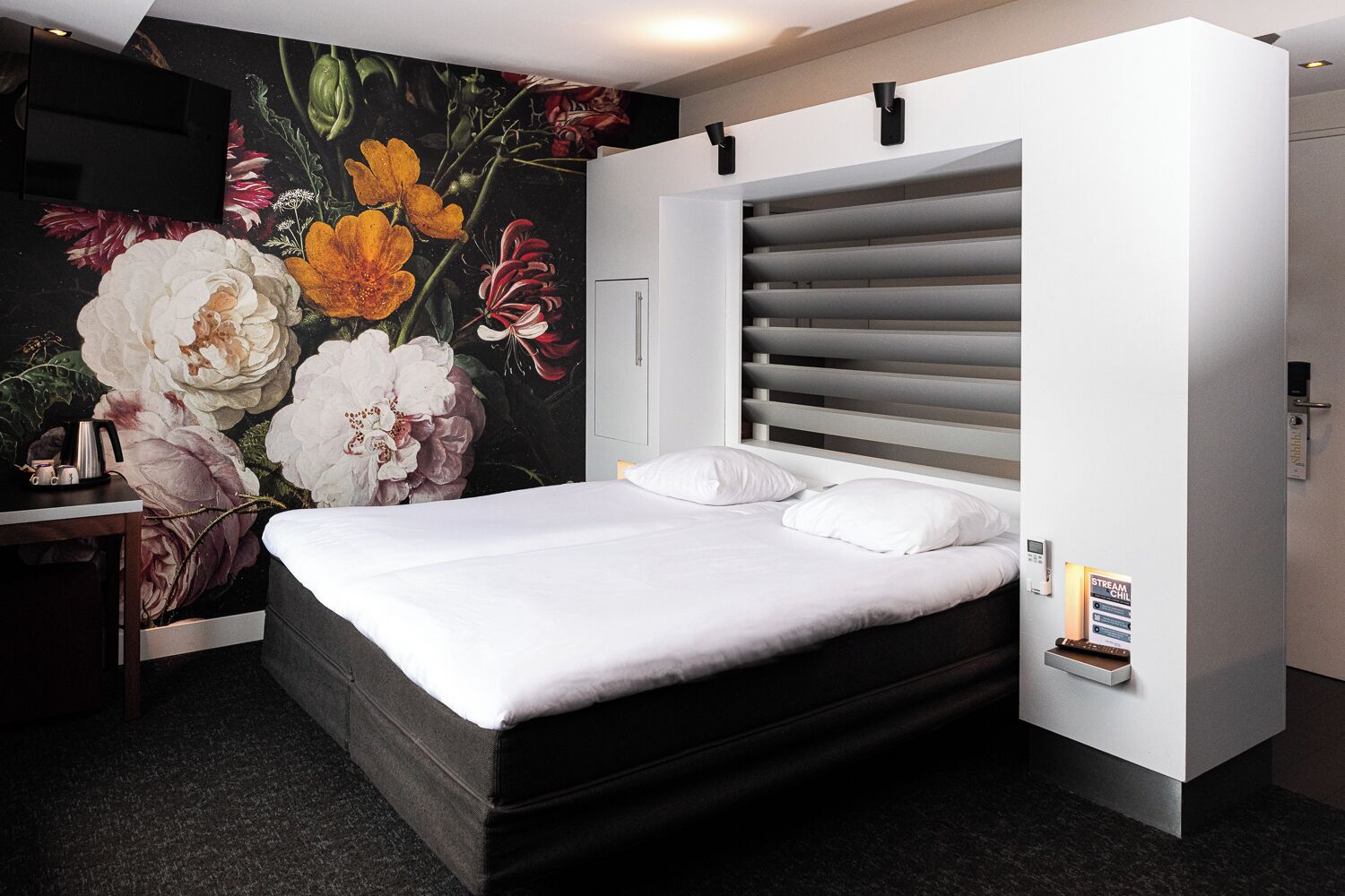 Een moderne hotelkamer met een groot bed, een wandtelevisie en een bloemenmural.