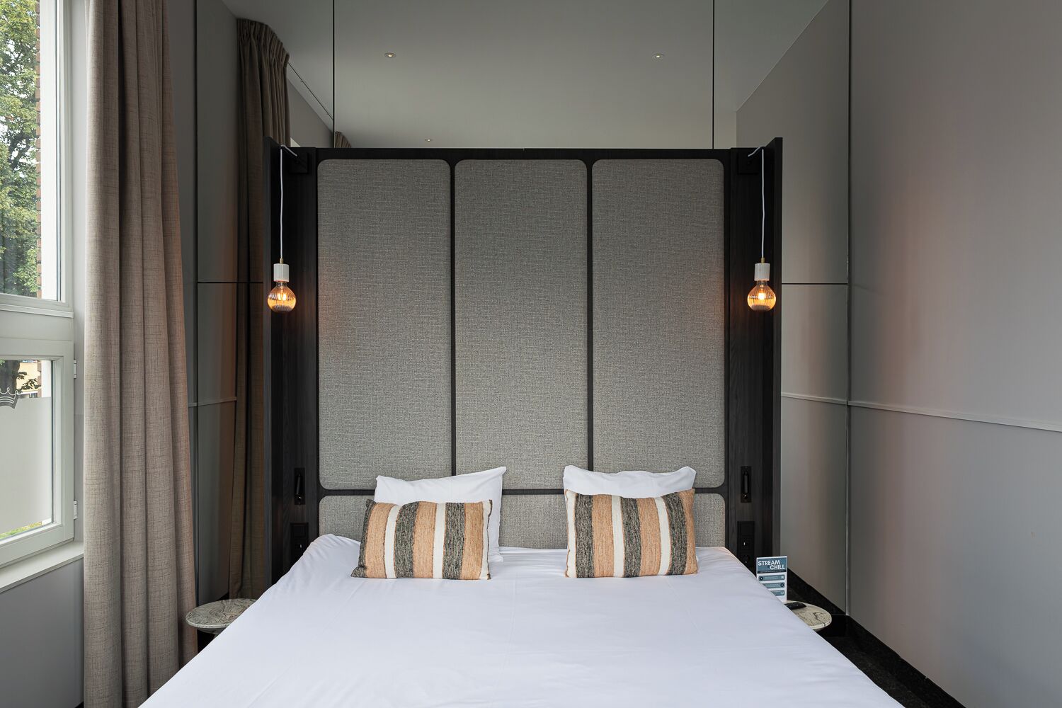Une chambre d’hôtel moderne avec un grand lit, deux oreillers, une tête de lit dotée de panneaux verticaux et deux lampes fixées au mur.