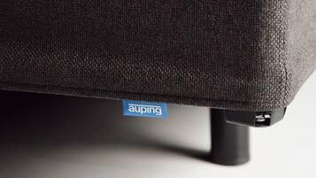 Een detail van een stoel met een stoffen textuur en een blauw label met de tekst 'auping'.