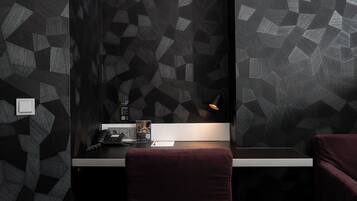 A modern hotel room with geometric patterned walls, a desk with a phone and a QR code, and a red chair.