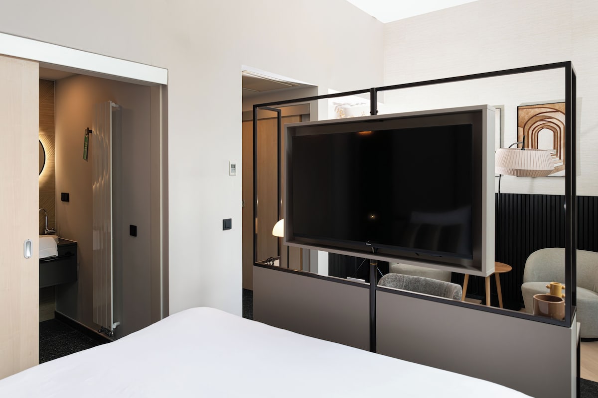 A hotel room with a bed, a TV, a desk, a chair, and a bathroom.