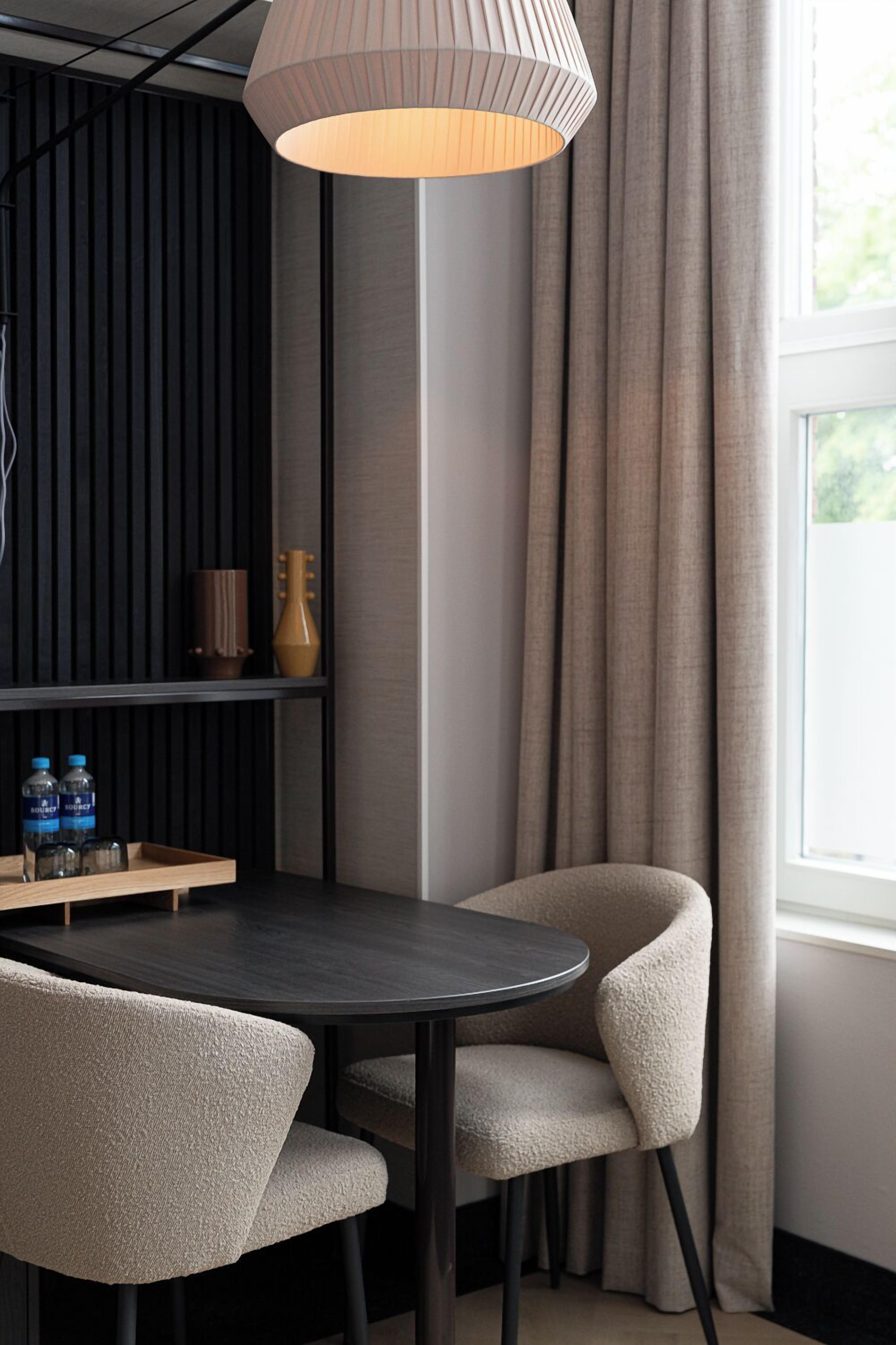 A modern dining area with a round table, two chairs, a pendant light, and a shelf with bottles.
