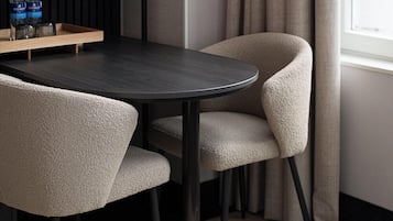 A modern dining area with a round table, two chairs, a pendant light, and a shelf with bottles.