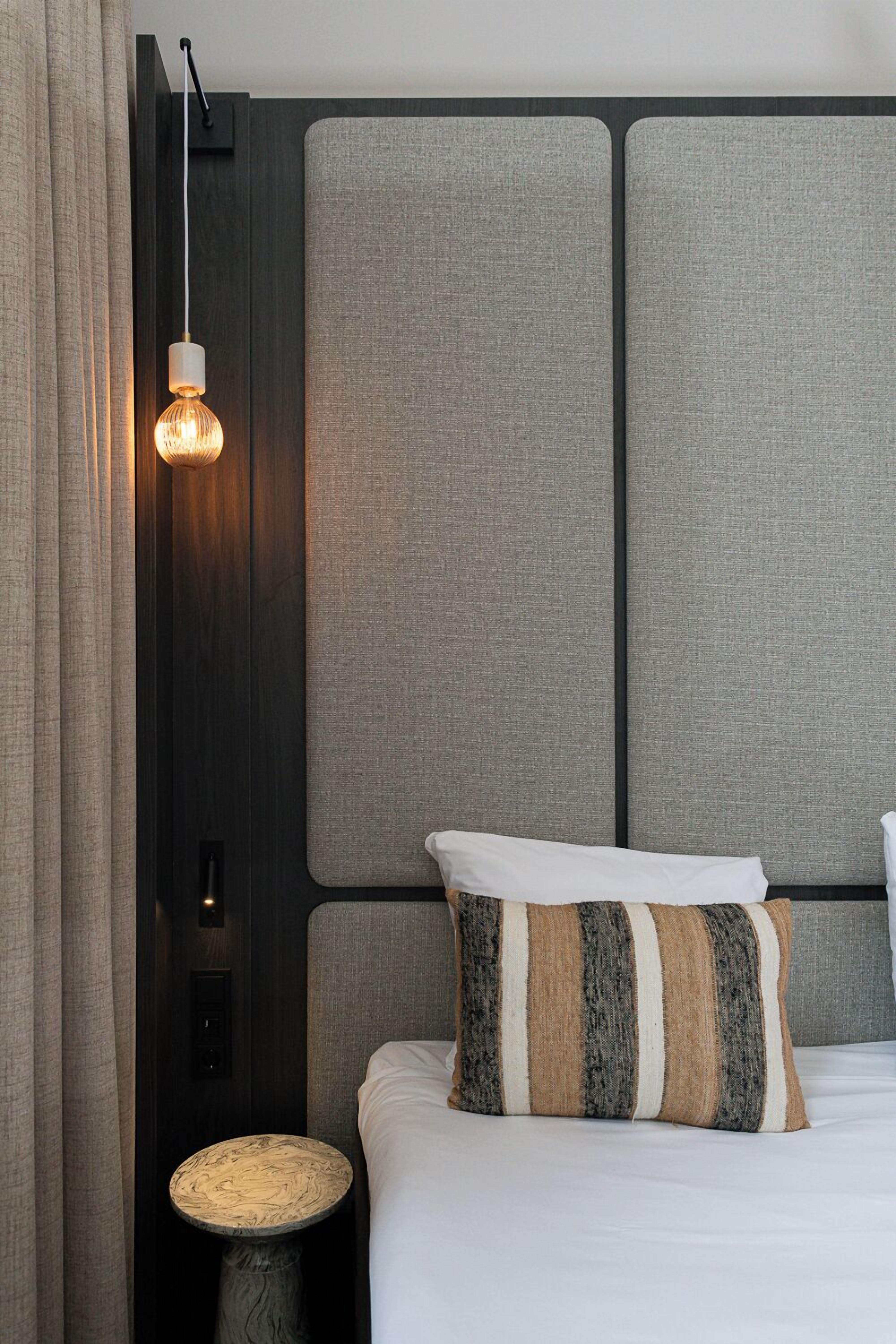 A modern hotel room with a large bed, a textured headboard, a bedside lamp, and a round side table.
