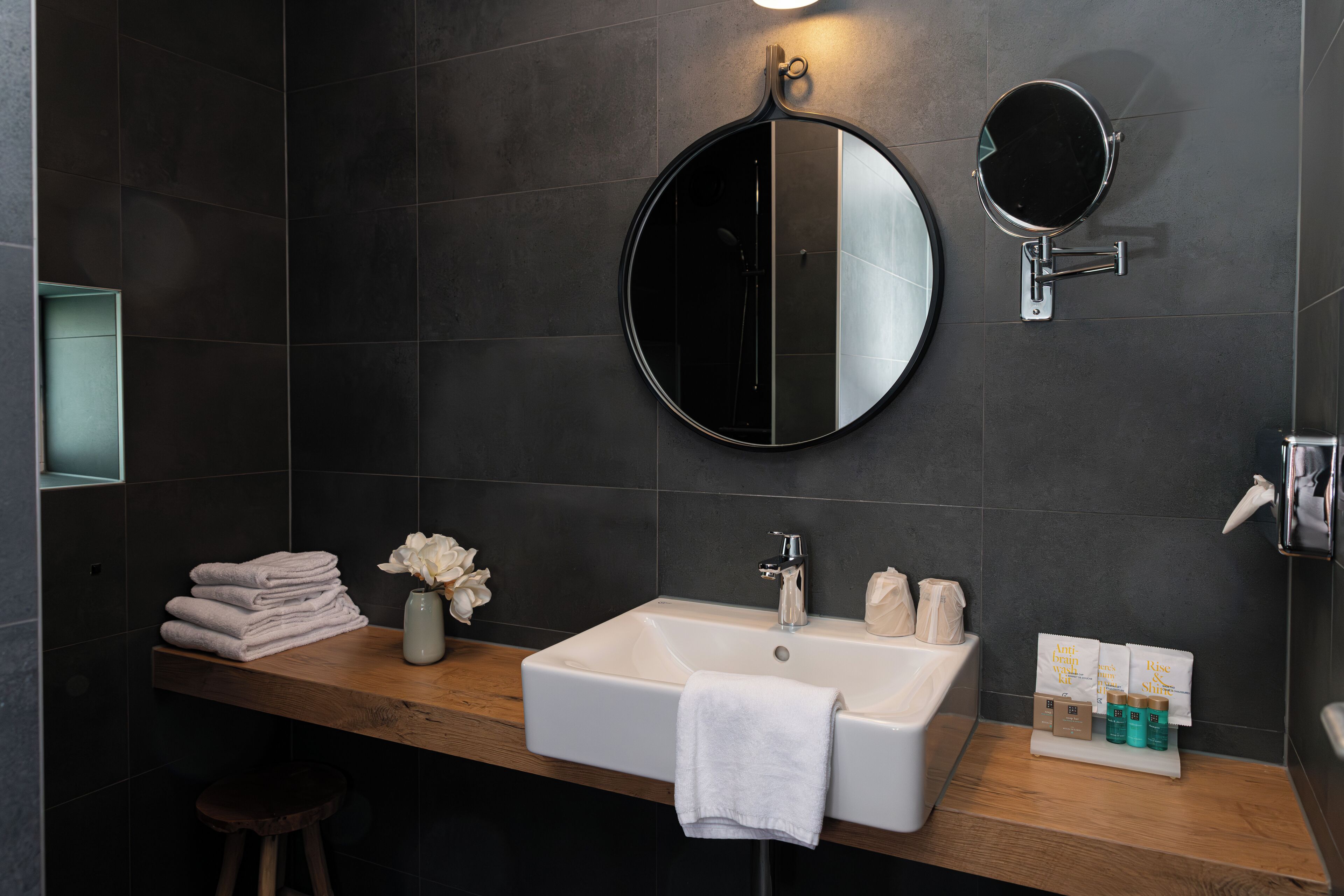 A modern bathroom with a wooden vanity, a round mirror, a white sink, and a towel rack.