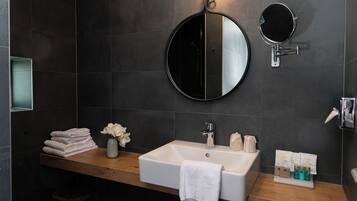 A modern bathroom with a wooden vanity, a round mirror, a white sink, and a towel rack.