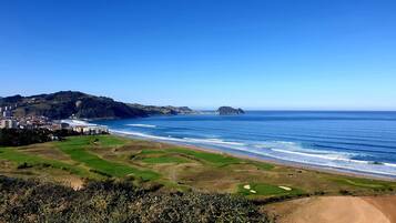 Paisagem costeira com campo de golfe, praia e uma cidade ao fundo.