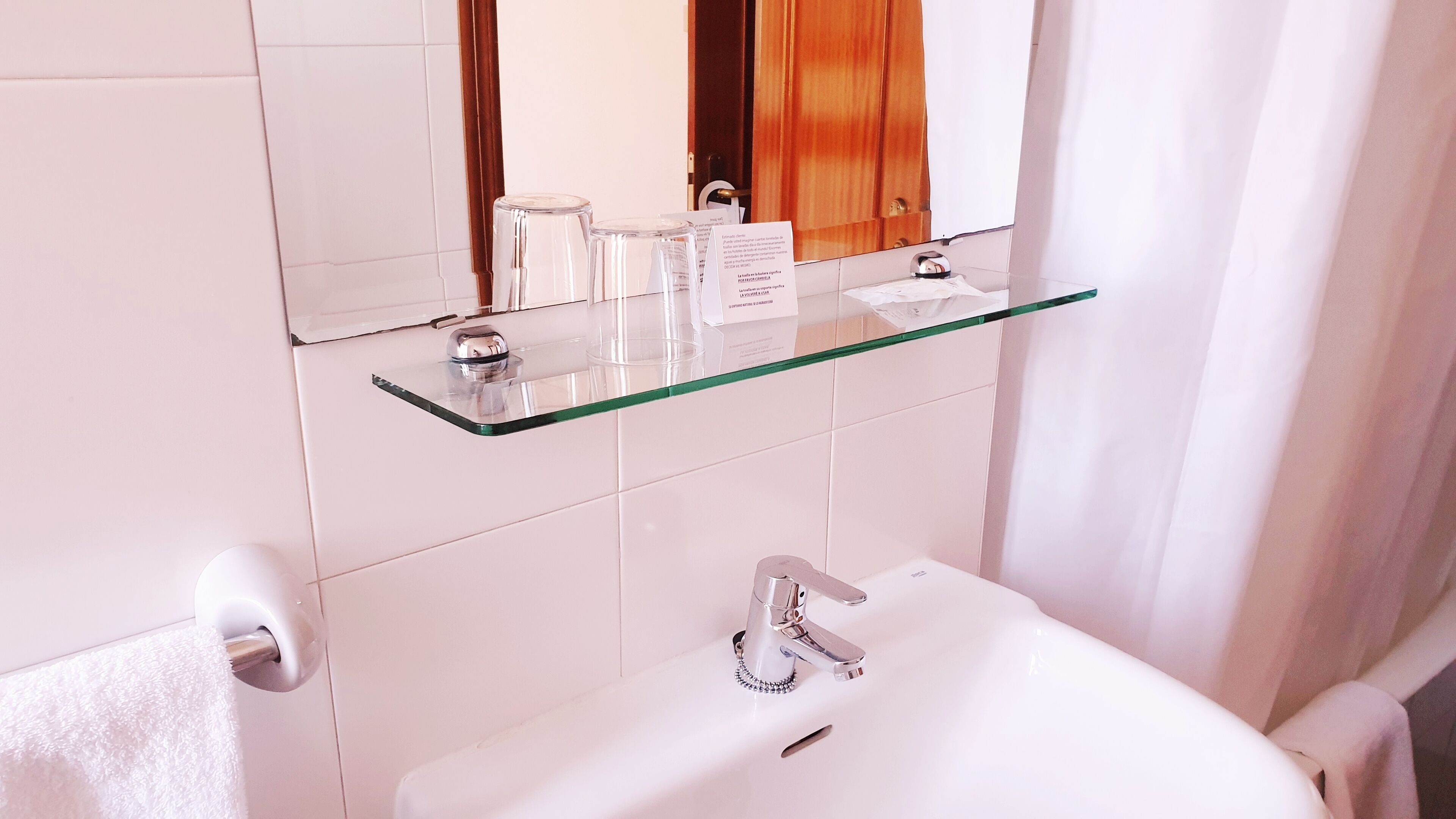 A bathroom with a glass shelf holding toiletries, a sink with a faucet, and a towel hanging on a rack.