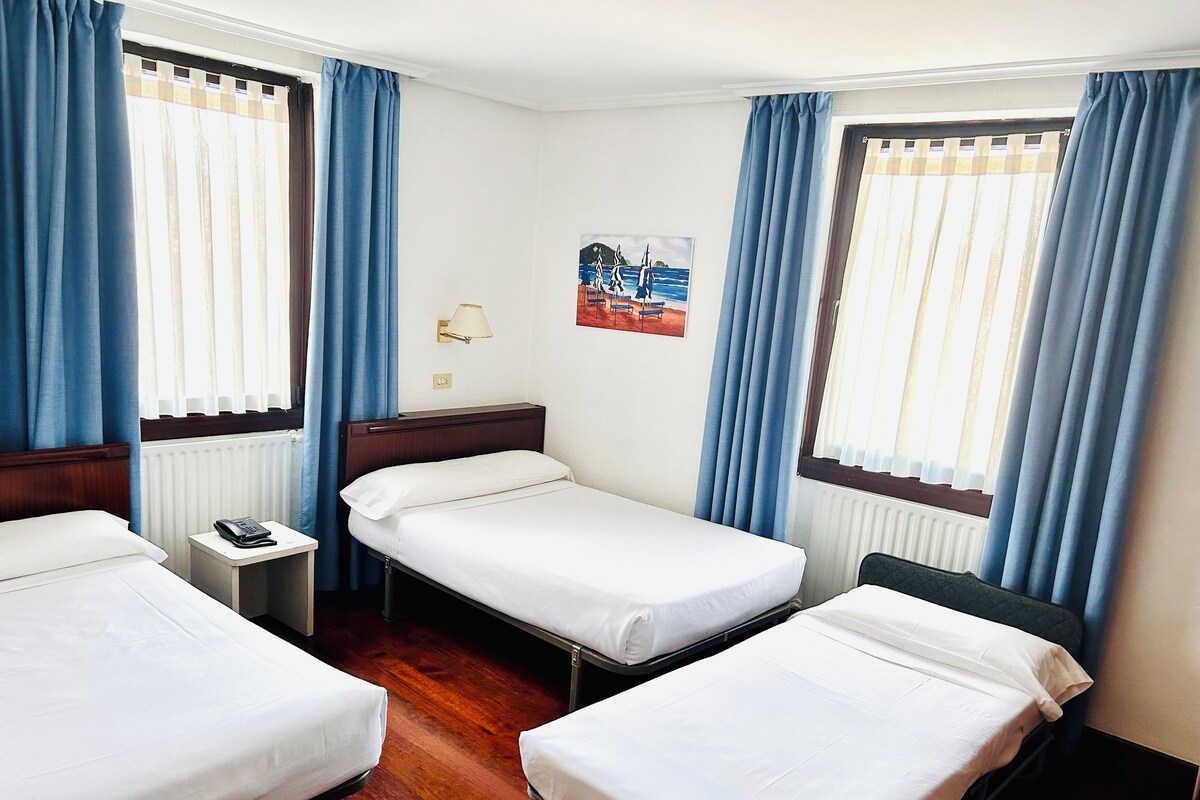 A hotel room with two single beds, a bedside table with a lamp, a small table with a phone, and a poster on the wall.