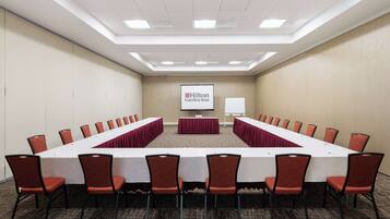 A conference room with a long table, red chairs, a whiteboard, and a Hilton Garden Inn sign.