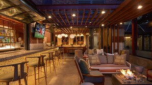 A bar area with stools, a sofa set, a fire pit, and a television mounted on the wall. - Hilton San Diego Gaslamp Quarter (San Diego)