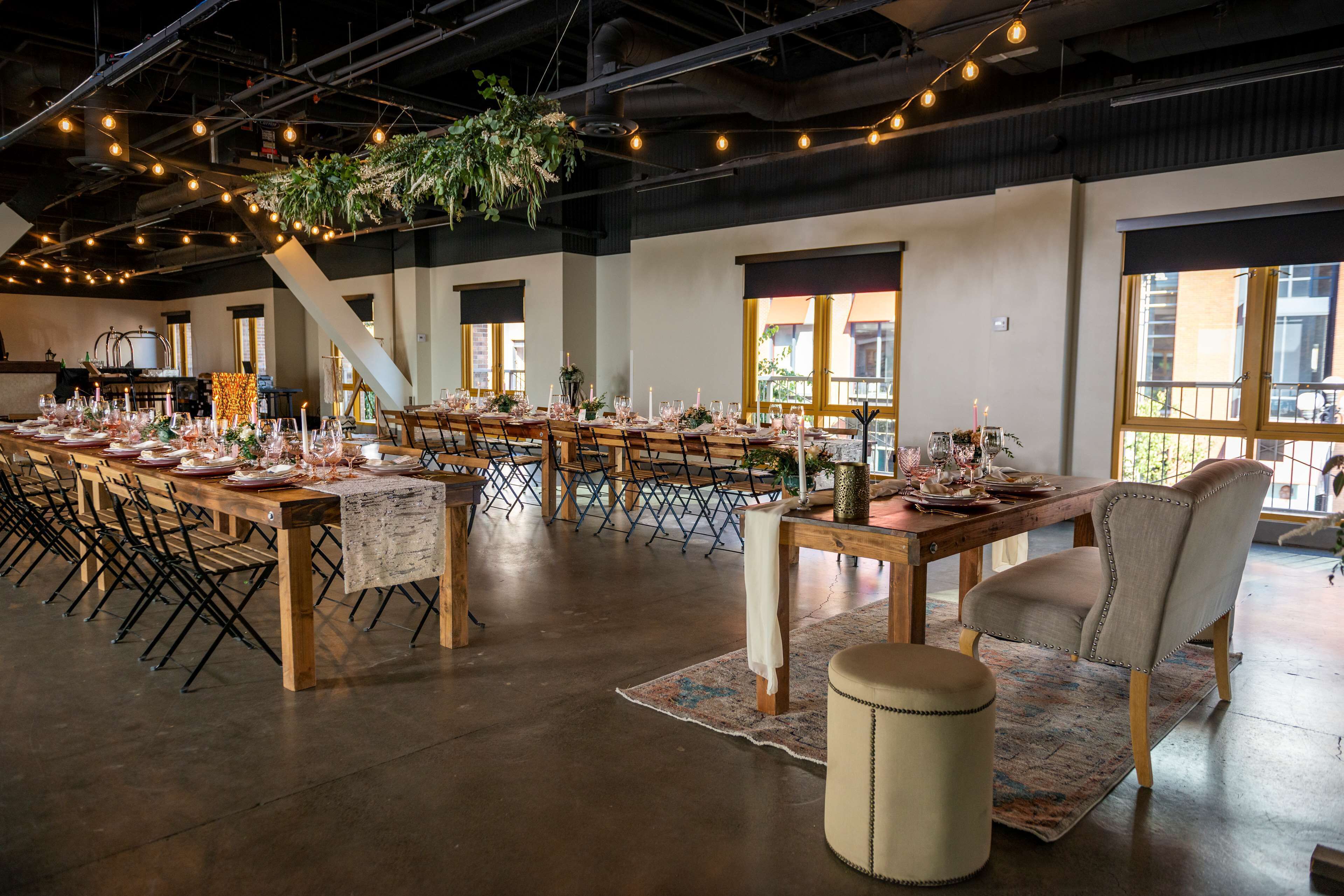 A spacious hall with long tables set for dining, wooden chairs, and hanging plants.