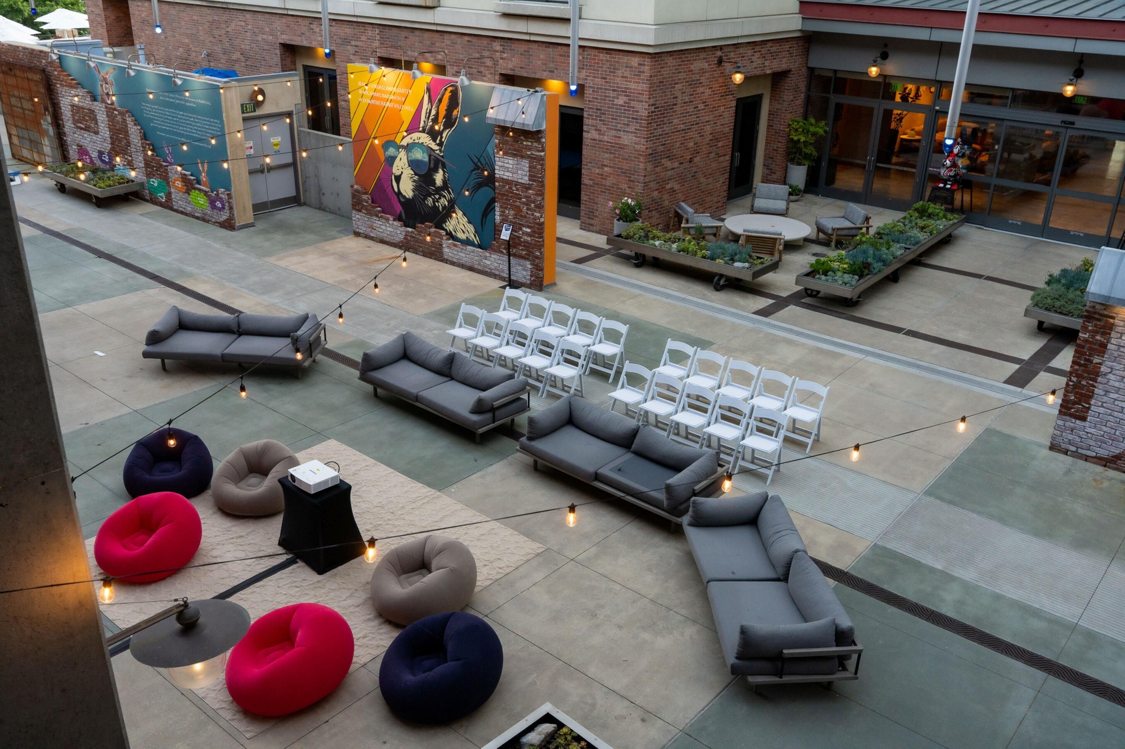 Un espacio al aire libre con varios sofás y sillones, un mural en la pared y luces colgantes.