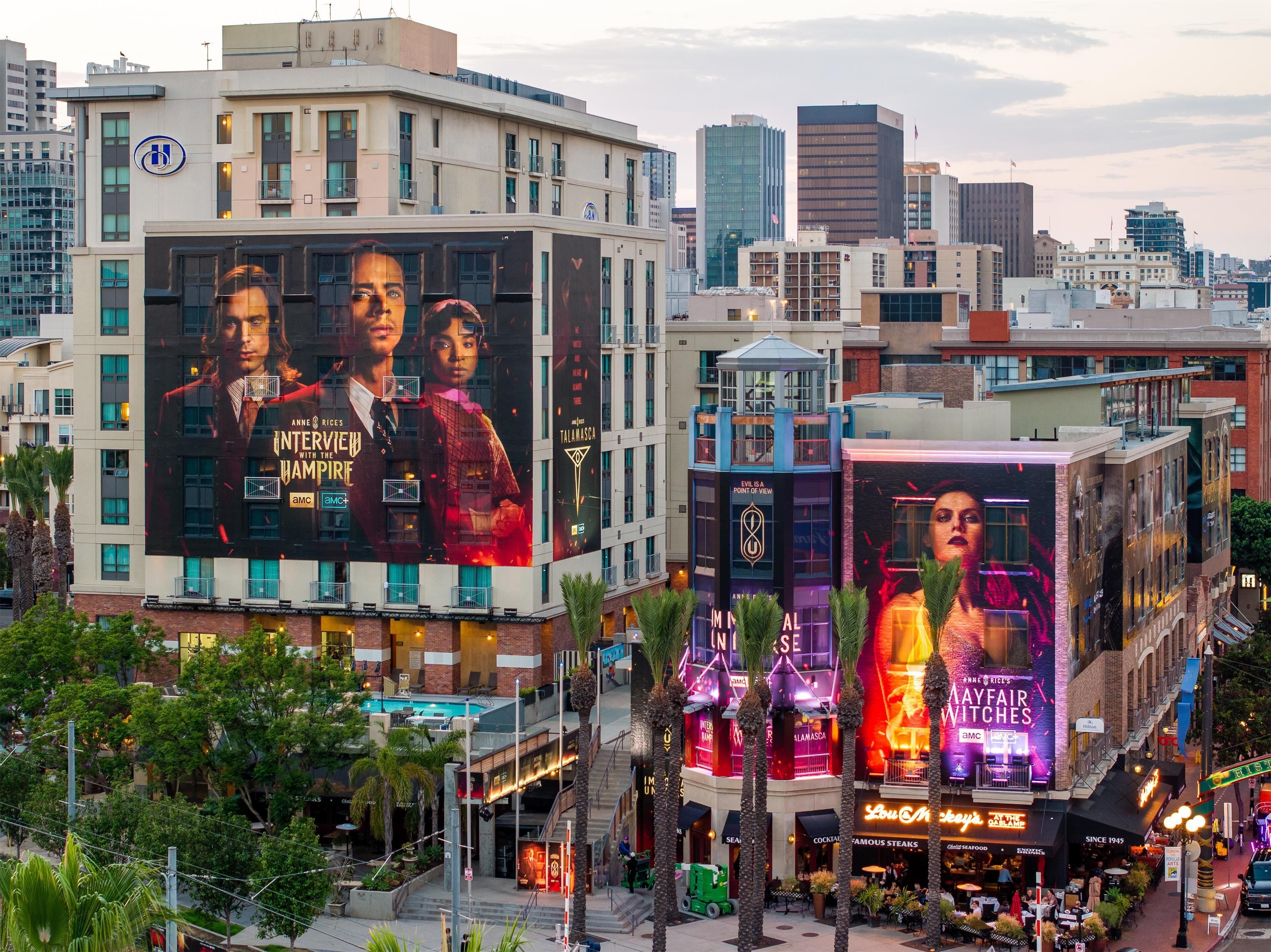A cityscape with modern buildings, including a prominent billboard advertising a TV show.