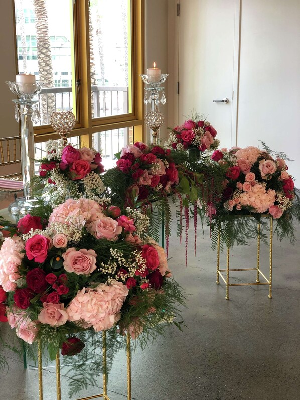 A room with large windows, a chandelier, and floral arrangements on stands.
