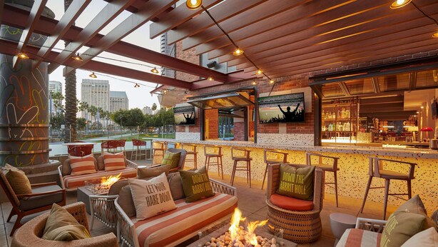 A cozy outdoor seating area with wicker furniture, a fire pit, and a bar with a city view. - Hilton San Diego Gaslamp Quarter (San Diego)