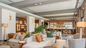 A spacious living area with a large sectional sofa, a coffee table, and a seating area with armchairs. There is a bar area in the background with stools and a television. - Hilton San Diego Gaslamp Quarter (San Diego)