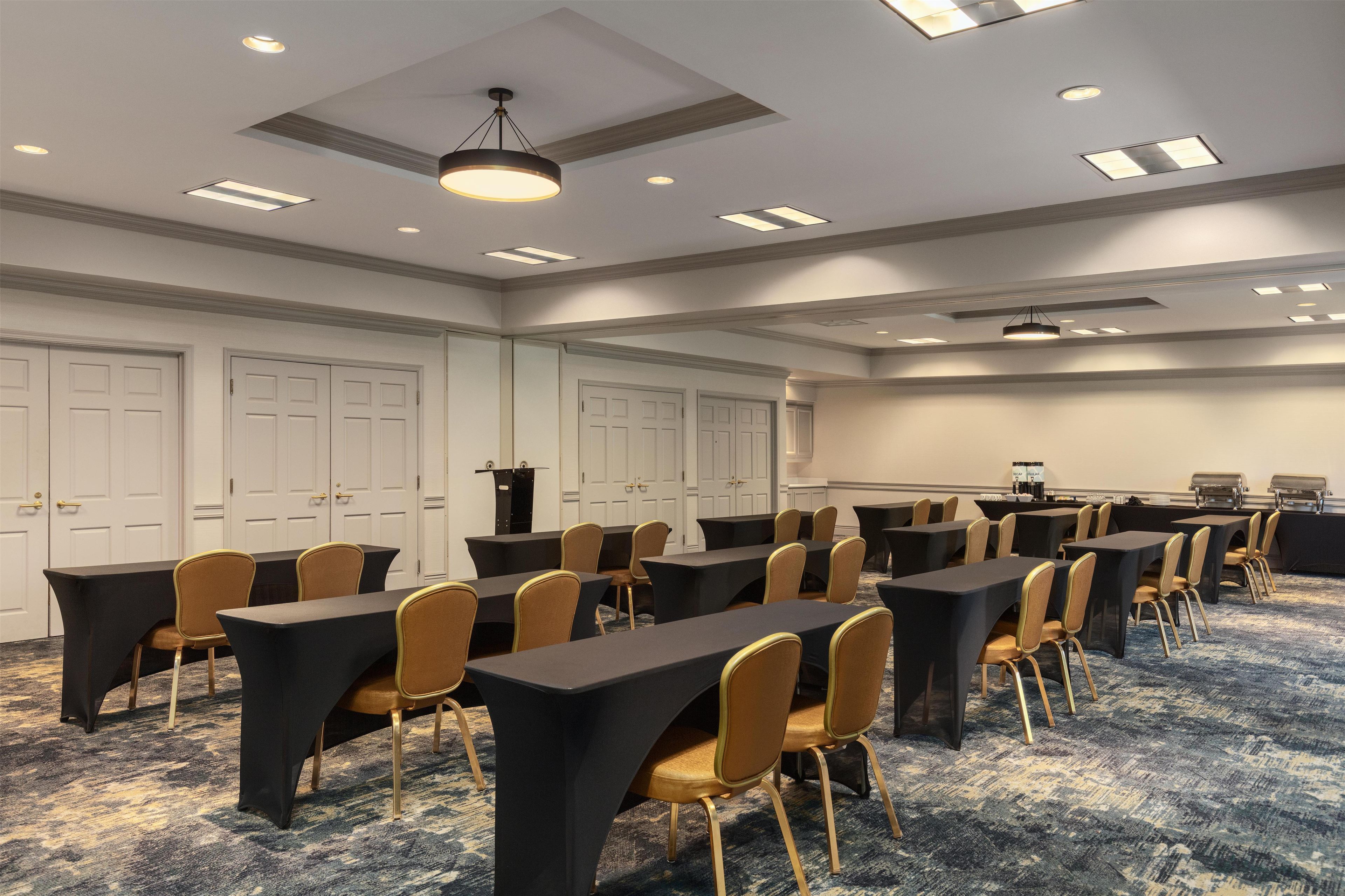 A conference room with tables and chairs, a carpeted floor, and a ceiling with recessed lighting.