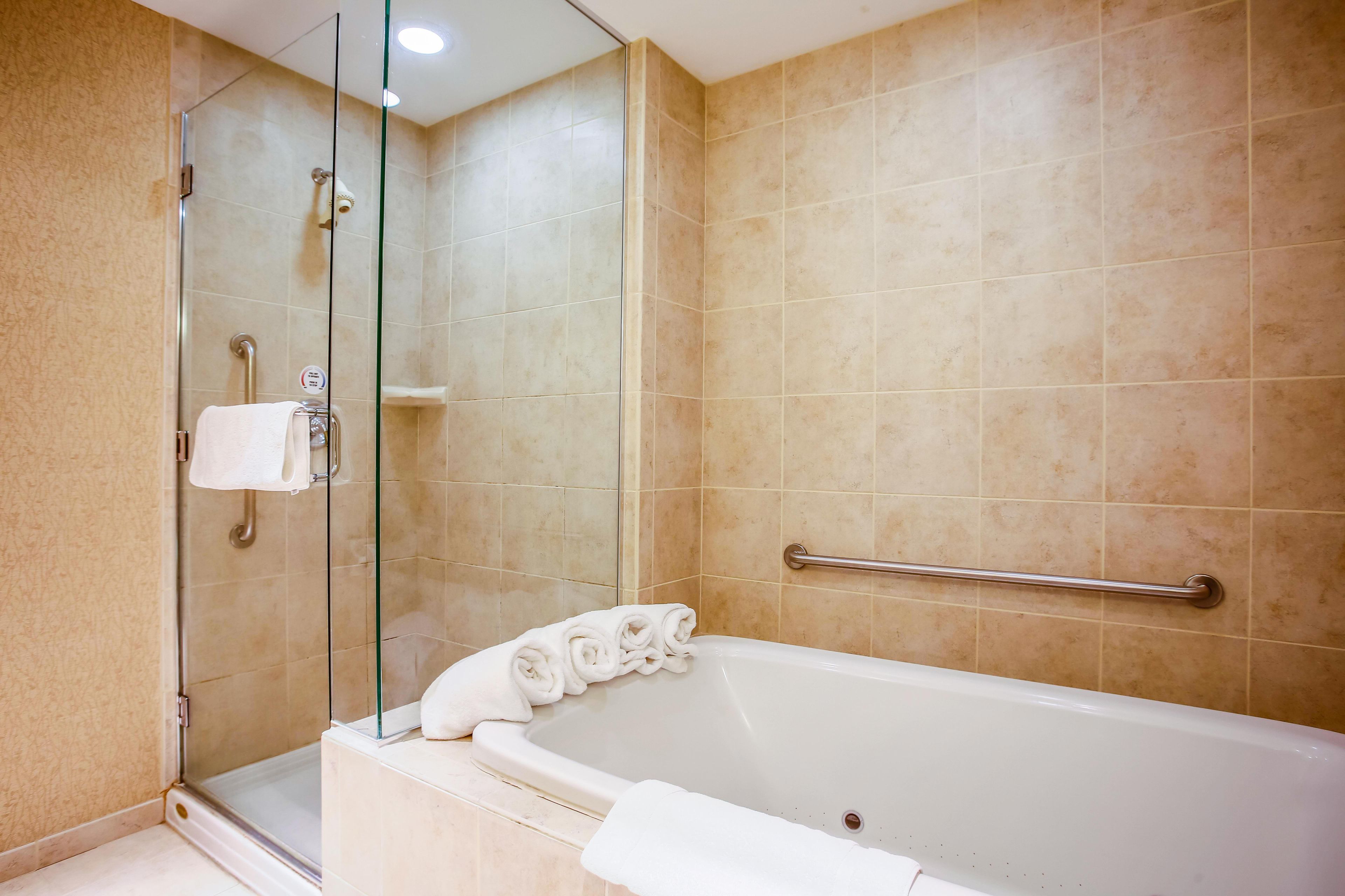 A bathroom with a bathtub, a glass shower enclosure, and a handrail.